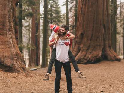 Man wearing "National parks are for lovers" shirt carrying woman on his back